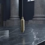 Brass plumb line, square, and gauge marks on a dark civic policy desk.
